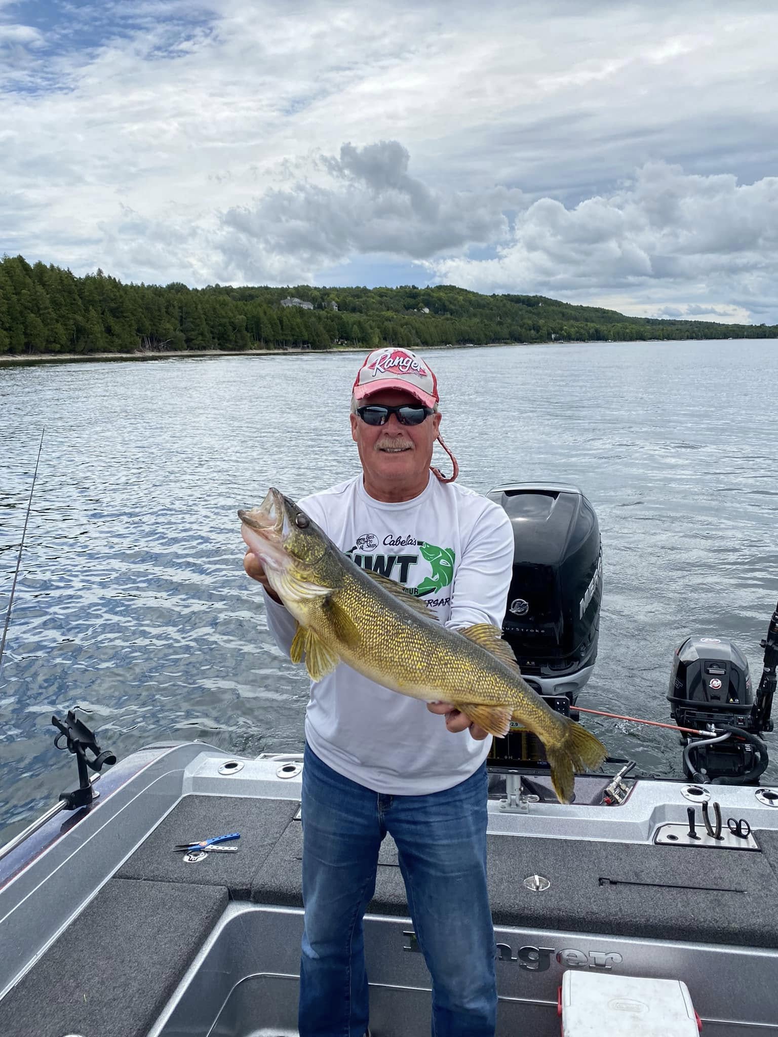 Wayne Butz holding a walleye on the lake with treeline in background